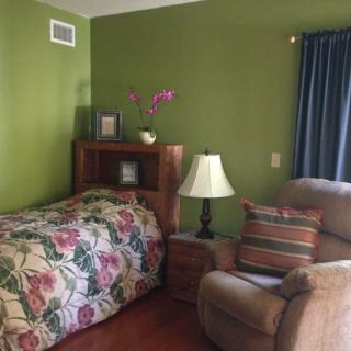 A cozy bedroom with green walls, featuring a floral bedspread, wooden furniture, and a comfortable armchair.