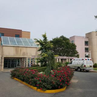 A view of a hospital with landscaped gardens and a cloudy sky.
