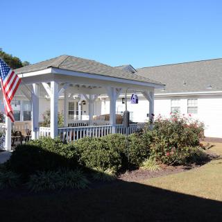 A white building with a covered patio and an American flag, set in a landscaped outdoor area.