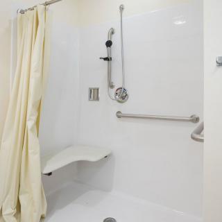 An accessible shower with grab bars, a folding seat, and a shower curtain.