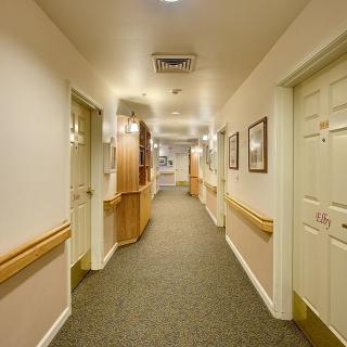 A well-lit hallway with handrails, carpeted floor, and multiple doors on either side.