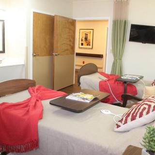 A hospital room with two beds, red blankets, and a television.