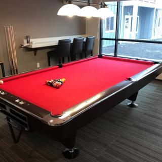 A red-felt pool table set up in a modern game room with cue sticks and overhead lighting.