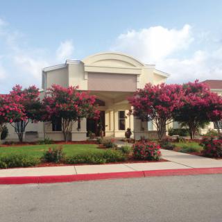 A well-landscaped building entrance with flowering trees and a cloudy sky.