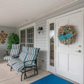 A cozy porch featuring striped cushioned chairs and a door adorned with a 'welcome' wreath.