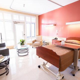 A clean and bright hospital room with a bed, furniture, and large windows.