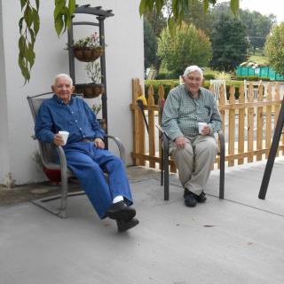 Two elderly men enjoying coffee on a patio.