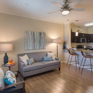 A modern open-concept living room with a view of the kitchen, featuring stylish decor and wood flooring.