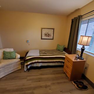 A cozy and well-lit bedroom featuring a single bed, a comfortable sofa, and a wooden nightstand with a lamp.