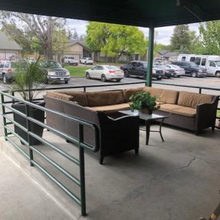A cozy outdoor seating area on a covered patio with couches and potted plants, overlooking a parking lot.