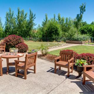 A serene backyard patio with wooden furniture surrounded by lush greenery.