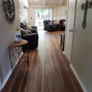 A view of a hallway leading to a living room with wooden flooring and comfortable seating.