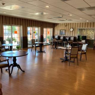 A neatly arranged dining area with tables and chairs on a wooden floor, featuring decorated walls and large windows.