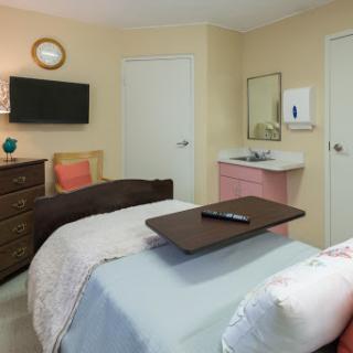 A cozy and well-equipped hospital room with two beds, a television, and a sink area.