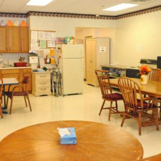 A communal kitchen and dining area with tables, chairs, a refrigerator, and wooden cabinets.