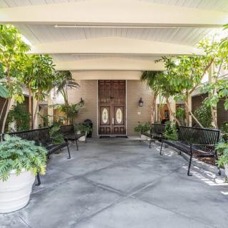 A covered entrance with benches and lush greenery leading to a set of wooden doors.