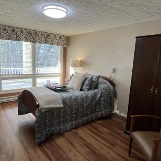 A cozy bedroom featuring a comfortable bed, wooden flooring, and ample natural light from the windows.