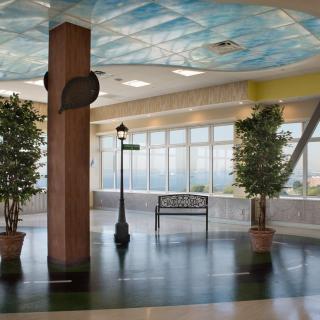A spacious indoor atrium with potted trees, a bench, and a streetlamp under a decorative ceiling.