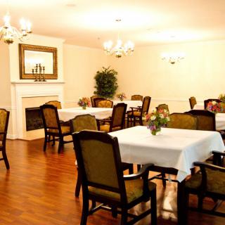A cozy dining room with elegantly arranged tables and chairs, featuring a fireplace and decorative lighting.
