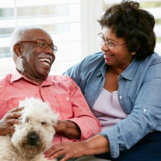 A happy elderly couple sharing a moment with their pet dog indoors.