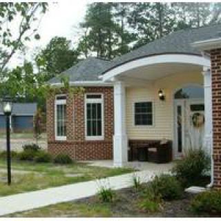 A small residential building with a brick facade, surrounded by a garden and pathway.