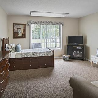 A cozy bedroom with a bed, dresser, and television next to a large window.