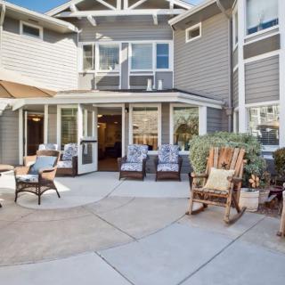 A cozy patio area with outdoor seating and a rocking chair, set against the backdrop of a house on a sunny day.