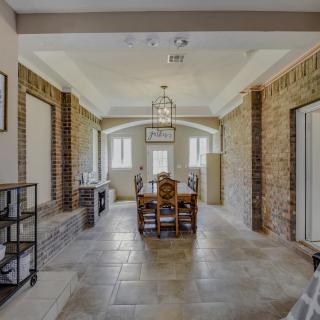 A stylish dining room with exposed brick walls, a central wooden table set under a decorative ceiling light, and large windows allowing natural light to fill the space.
