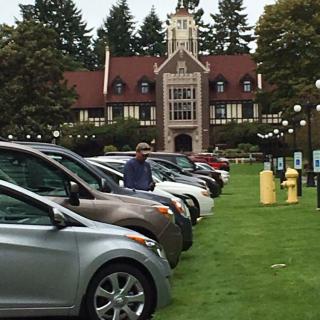 A row of parked cars in front of a historic building surrounded by trees.