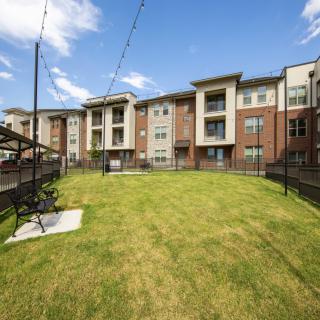 A modern apartment complex with a well-maintained lawn and outdoor amenities under a clear blue sky.
