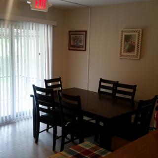 A cozy dining room with a dark wooden table and chairs, complemented by framed artwork and natural light from a sliding glass door.
