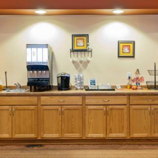 A well-organized breakfast area featuring a coffee station and beverage dispenser on a wooden counter with artwork above.