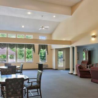 Spacious living area with tables and chairs, featuring large windows and natural lighting.