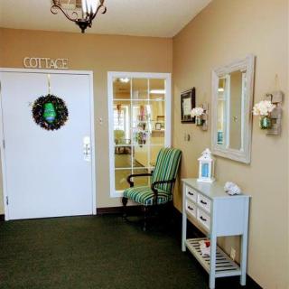 A welcoming entryway with a decorated door, a chair, and a small table with a mirror and lamp.