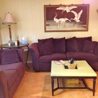 A cozy living room with a purple sofa, matching armchair, and a coffee table, featuring wall art and a floor lamp.