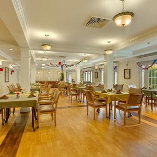 A spacious dining room with elegantly arranged tables and chairs, featuring warm lighting and wooden flooring.