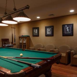 A cozy billiards room featuring a pool table, comfortable seating, and stylish wall art under warm lighting.