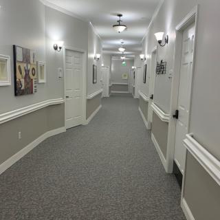 A well-lit, carpeted hallway with several doors and decorative wall art.