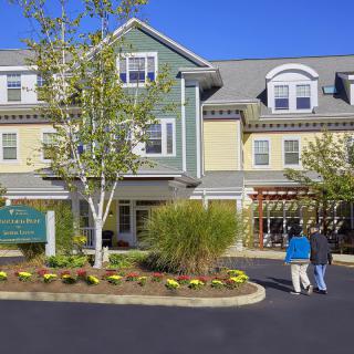 A residential building with a landscaped entrance on a sunny day, where two people are walking.