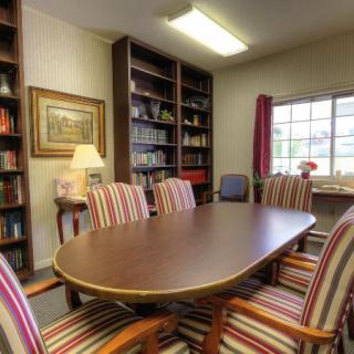 A cozy conference room with a wooden meeting table, striped chairs, and bookshelves by the window.