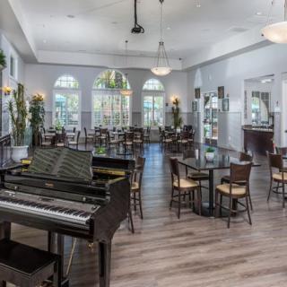 A spacious and elegant dining area featuring a piano, modern furnishings, and large windows with ample natural light.