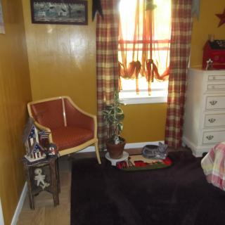 A cozy room corner featuring a chair, potted plant, and window with colorful curtains.