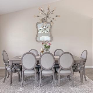 A modern dining room with a large table, elegant chairs, a decorative chandelier, and a stylish mirror.