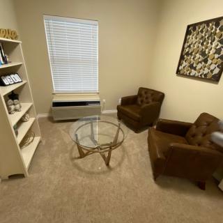 A cozy living room with two armchairs, a glass coffee table, and a bookshelf on a carpeted floor.