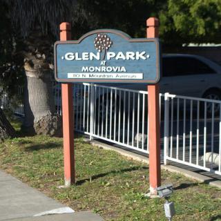 A sign for Glen Park in Monrovia, located near a sidewalk and fence, with trees in the background.