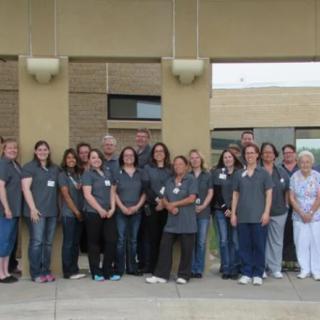 A group of people standing together outside, wearing casual shirts.