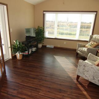 A cozy living room with hardwood floors, featuring a large window, plants, and comfortable furniture.