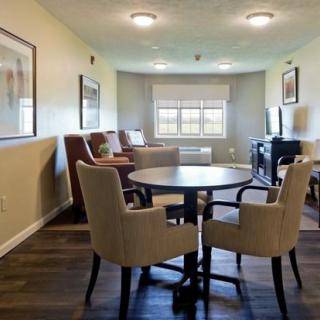 A cozy living room with a round table and chairs, featuring ample natural light from a large window.