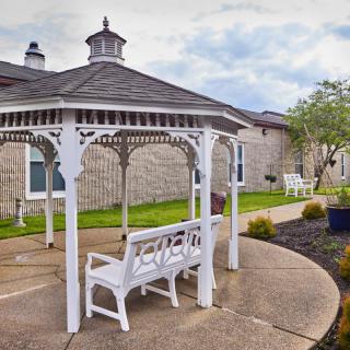A peaceful garden setting featuring a white gazebo and benches on a paved walkway.