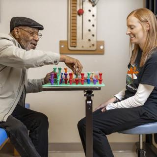 An elderly man and a young woman play chess together indoors.